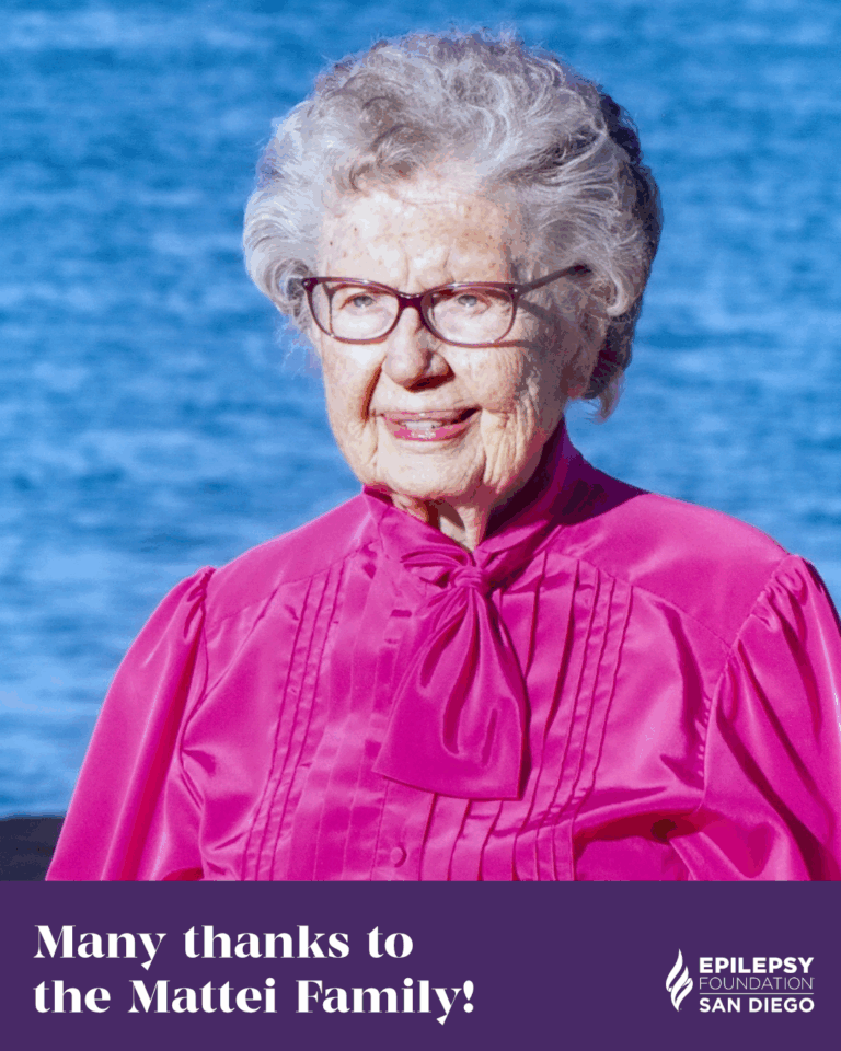 A daytime color photo of the late Ruth S. Mattei, posing for a photo in a long-sleeve fuschia blouse, with the ocean behind her. White text on a purple background is layered over the bottom of the photo, and reads, "Many thanks to the Mattei family!" The white logo of the Epilepsy Foundation of San Diego County appears in the bottom right corner of the graphic.